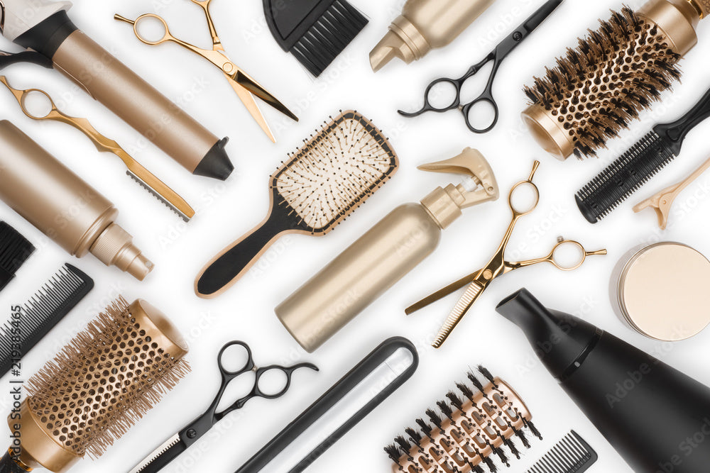 a collection of professional hair styling tools arranged on a white surface. The set includes various items such as hairbrushes, curling irons, shears, and spray bottles. 