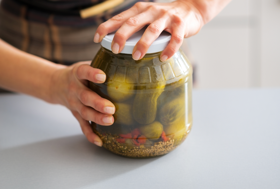 a person attempting to open a glass jar of pickles